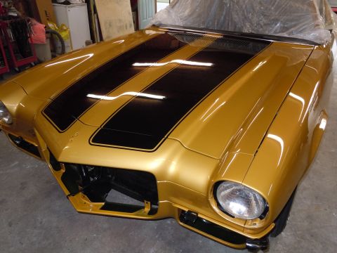 1970 Chevrolet Camaro - Front view of a gold 1970 Chevrolet Camaro with black racing stripes, showing its distinctive body style.