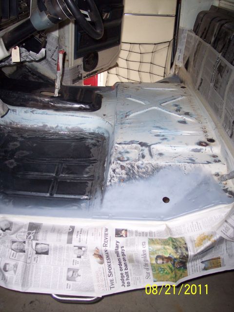 1973 Ford F-250 - The interior floor pan of a vehicle is covered with newspaper, revealing primer and areas needing repair.