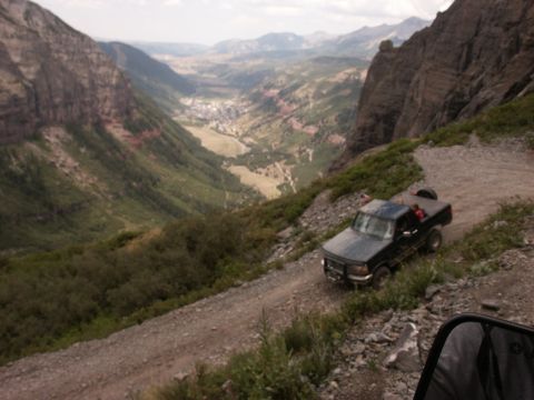 1995 Ford Bronco - A Ford F-Series truck navigates a steep, winding dirt road with a scenic valley below.