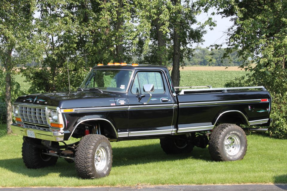 1979 Ford F-250 pickup truck, lifted with large tires, parked on grass with trees in background