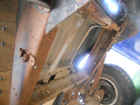 1991 Ford Bronco - Underside view of heavily rusted vehicle frame and suspension components, showing leaf springs and a tire.