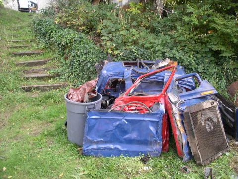 1979 Ford Bronco - Disassembled car body parts are piled up on the grass next to a trash can.