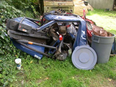 1979 Ford Bronco - A jumbled collection of vehicle components sits in a grassy area, with a large gray trash can nearby.