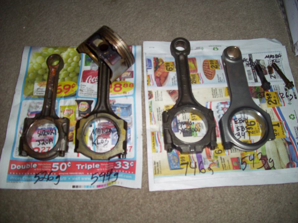 Four engine connecting rods, one with a piston attached, laid out on newspapers