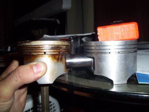 1995 Ford Probe - Comparison of a used piston with carbon buildup next to a clean, new piston, with an orange cap on top of the new one.