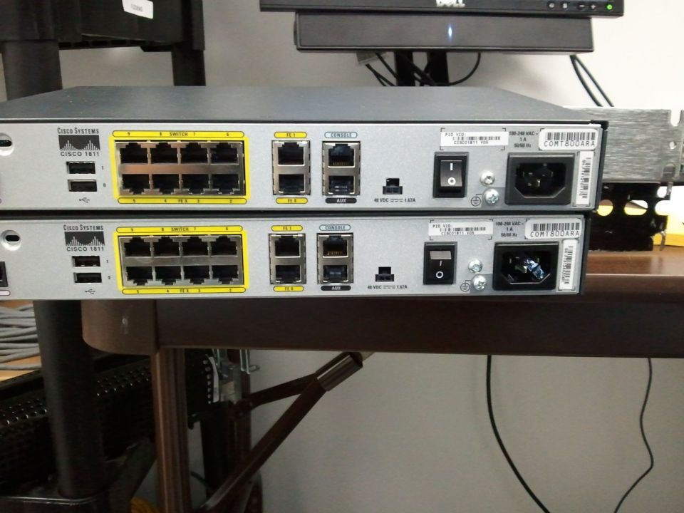 Two Cisco Systems 1811 routers stacked with yellow Ethernet ports