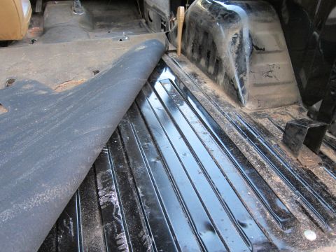 1987 Dodge 1500 - The interior floor of a vehicle is exposed, revealing ribbed metal beneath a lifted floor mat.