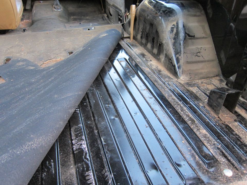 Interior of a vehicle with the floor mat peeled back, showing ribbed metal flooring