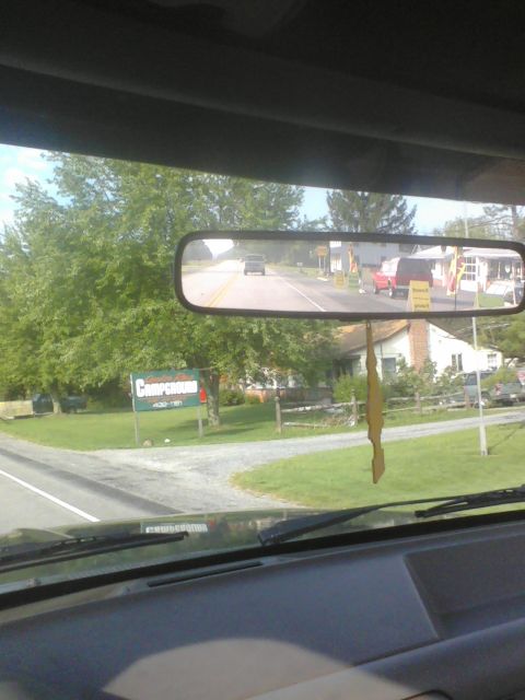 1988 Ford Bronco - A view from inside a vehicle shows a road with trees and houses, with other vehicles visible in the distance.