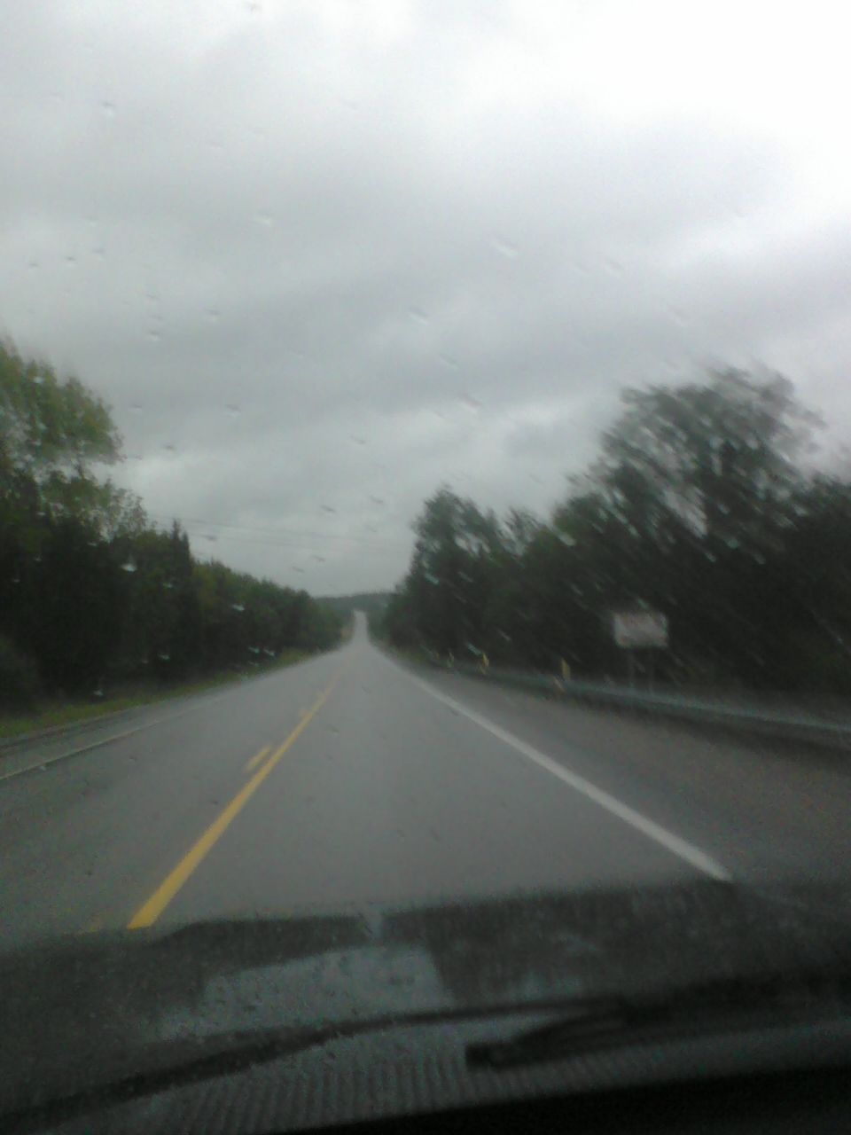 View from inside a vehicle looking out at a wet road under a cloudy sky