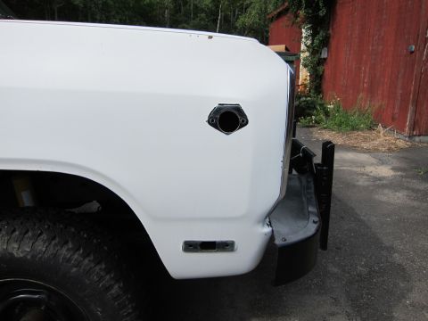 1987 Dodge 1500 - Close-up view of the front fender and tire of a white pickup truck, showing a circular opening and a side marker light housing.