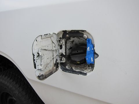 1987 Dodge 1500 - The fuel door on a white vehicle shows signs of wear and tear, with peeling paint and blue tape securing the cap.