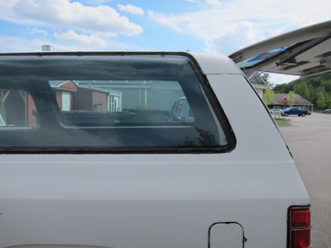 1987 Dodge 1500 - Rear view of a white van parked outdoors with a blue car visible in the distance.