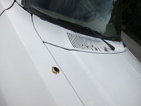 1987 Dodge 1500 - Close-up of a white truck's hood, showing a rusted hole and the windshield wiper area.