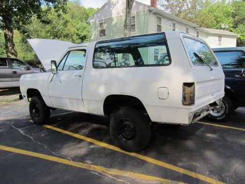 1987 Dodge 1500 - A white SUV is parked in a lot with its hood open and the rear bumper removed, showing exposed frame.