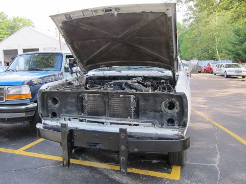 1987 Dodge 1500 - A white pickup truck sits in a parking lot with its hood open, revealing its engine compartment. Another truck is parked beside it.