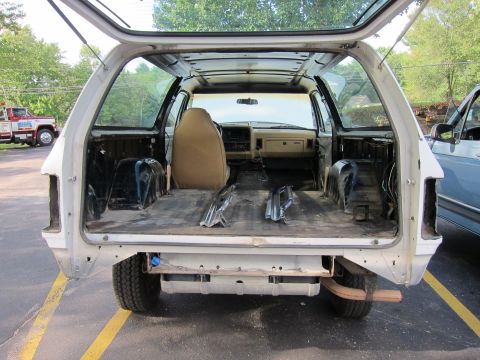 1987 Dodge 1500 - The interior of a white SUV is shown with its rear cargo area and cabin stripped down, revealing the frame and components.