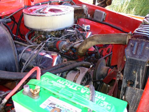 1979 Ford Bronco - The engine bay of a red 1979 Ford Bronco, showing the air cleaner, battery, and various engine components.