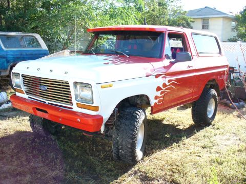 1979 Ford Bronco - This lifted Ford Bronco features custom flame decals and is parked in a grassy yard next to another Bronco.