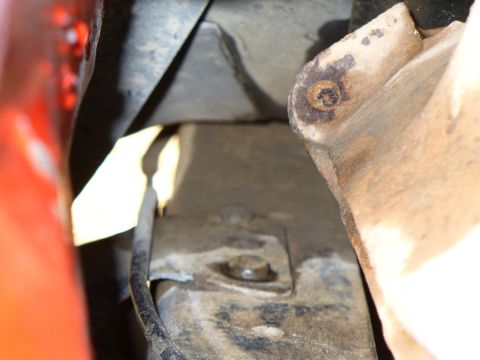 1979 Ford Bronco - Detail shot of a rusty metal bracket and bolt, with a hint of red paint visible on the left side.