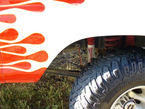 1979 Ford Bronco - Close-up of a vehicle's fender and tire, flame graphics and visible suspension parts.