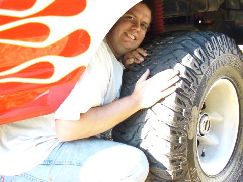 1979 Ford Bronco - A man poses with a large tire and flame decals on the side of a vehicle.