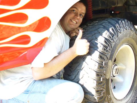 1979 Ford Bronco - Man poses with a large tire and flame decals on a vehicle.