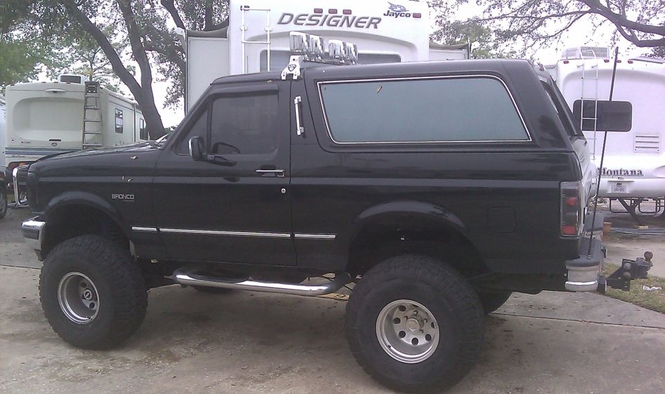 Black Ford Bronco with lifted suspension and aftermarket wheels. A "Bronco" badge is visible on the fender