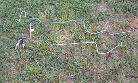 1979 Ford Bronco - Two sets of metal brake lines are laid out on the grass, one set appears new and silver, while the other is old and rusted.
