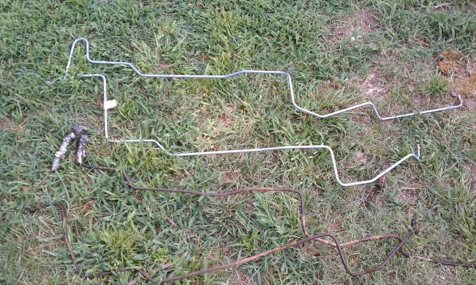Two sets of metal brake lines on grass, one set is silver and the other is rusted brown