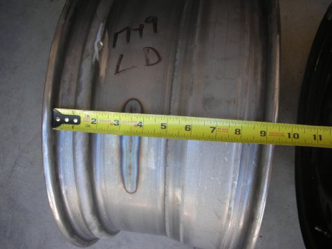 2004 Ford Crown Victoria - A tape measure is placed against a metal wheel rim, showing a measurement. Handwritten markings are visible on the rim's surface.