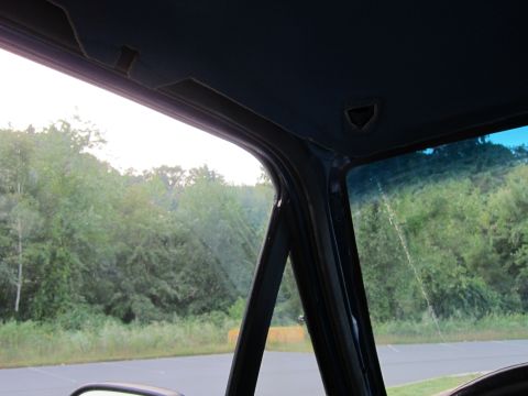 2001 Ford Crown Victoria - View from inside a vehicle's cabin, looking out through the windshield and side window at a tree line and asphalt ground.