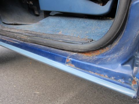 2001 Ford Crown Victoria - The lower door frame of a blue vehicle exhibits significant rust damage, indicating potential structural issues.