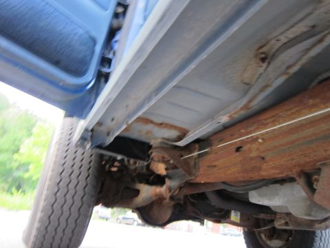 2001 Ford Crown Victoria - The underbody of a blue vehicle reveals significant rust on the frame and chassis components, with a tire visible on the left.