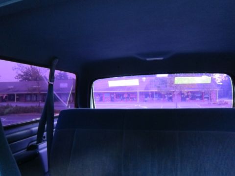 2001 Ford Crown Victoria - Looking through the tinted rear window of a vehicle at a row of shops in a strip mall.