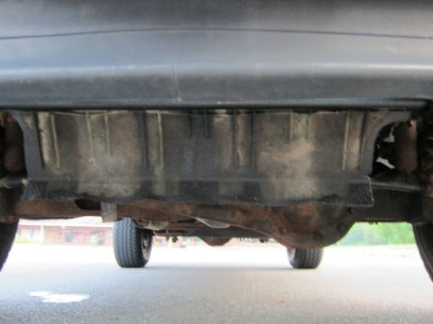 2001 Ford Crown Victoria - The underside of a vehicle reveals a black plastic shield and rusty components, with tires visible from a low angle.