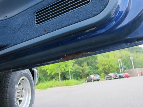 2001 Ford Crown Victoria - Rust is visible on the blue door sill of a vehicle, with other cars parked in the background.