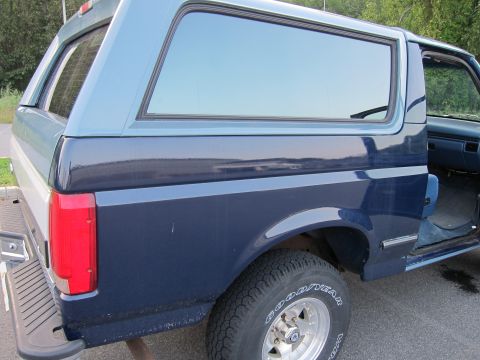 2001 Ford Crown Victoria - This is a side view of a blue two-tone Ford Bronco, a camper shell and an open driver's side door.
