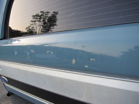 2001 Ford Crown Victoria - Close-up of a damaged light blue vehicle's rear quarter panel with a silver trim piece.