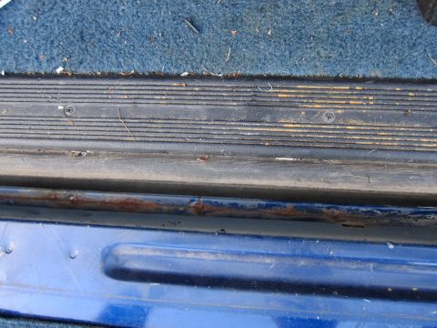 2001 Ford Crown Victoria - Close-up of a blue vehicle's interior door sill, showing wear and rust on the metal trim.