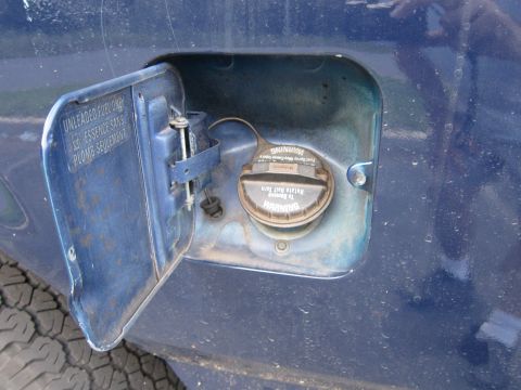 2001 Ford Crown Victoria - The fuel door of a blue vehicle is open, revealing the gas cap with warning labels.
