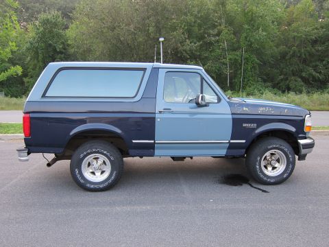 2001 Ford Crown Victoria - This two-tone Ford Bronco is parked on a paved surface with a line of trees behind it.