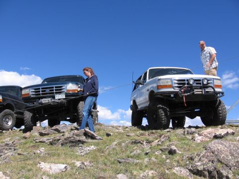 1995 Ford Bronco - Two Ford Broncos, including a white 1995 model with off-road modifications, are parked on a rocky slope under a blue sky.