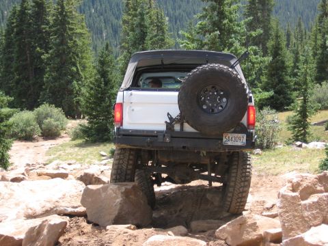 1995 Ford Bronco - This SUV navigates a challenging rocky path surrounded by pine trees.