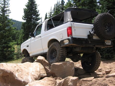 1995 Ford Bronco - This white Ford Bronco is shown off-roading on a rocky trail with a soft top and spare tire mounted on the rear.