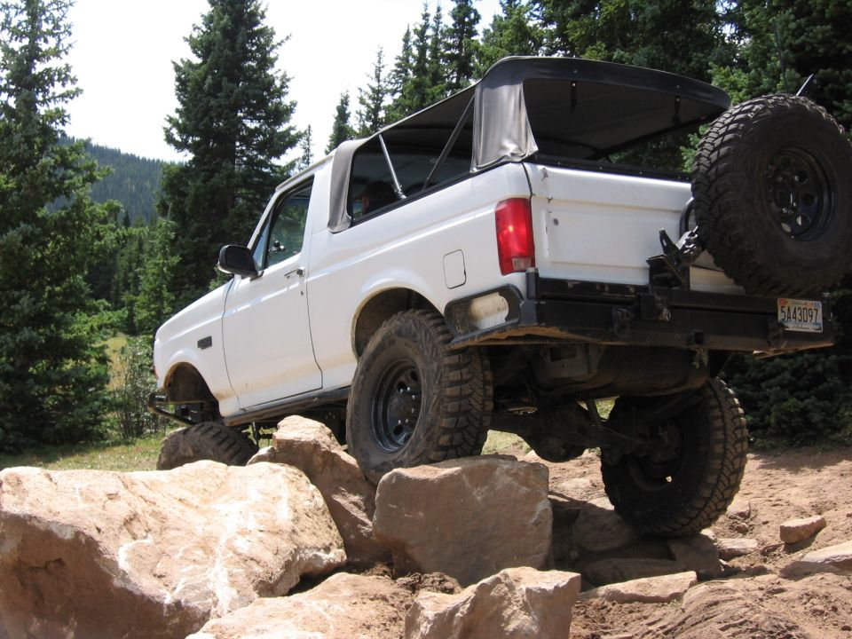 Lifted white Ford Bronco with soft top climbing boulders, rear spare tire carrier