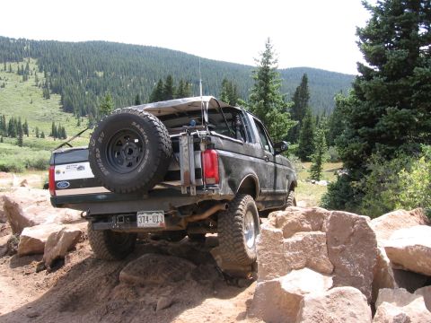 1995 Ford Bronco - A black 1995 Ford Bronco tackles a challenging rocky trail in a mountainous, forested area.