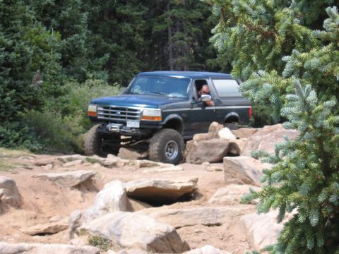 1995 Ford Bronco - A dark green Ford Bronco navigates a challenging rocky terrain, its lifted suspension clearly visible.