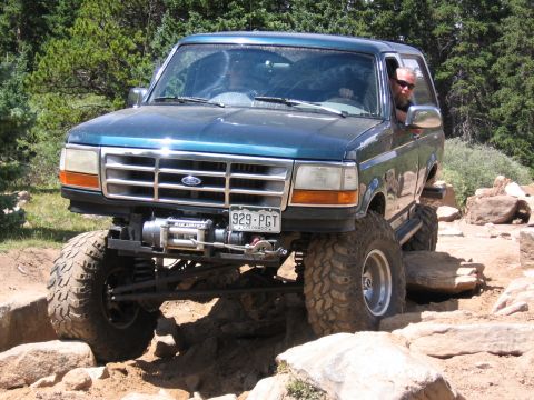 1995 Ford Bronco - Modified Ford Bronco driving on a challenging rocky trail with large tires and a winch.