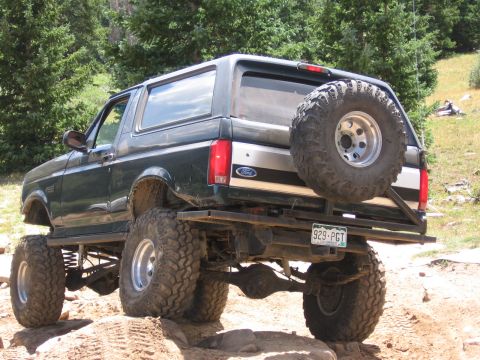 1995 Ford Bronco - This lifted Ford Bronco navigates a rocky, off-road trail surrounded by trees.